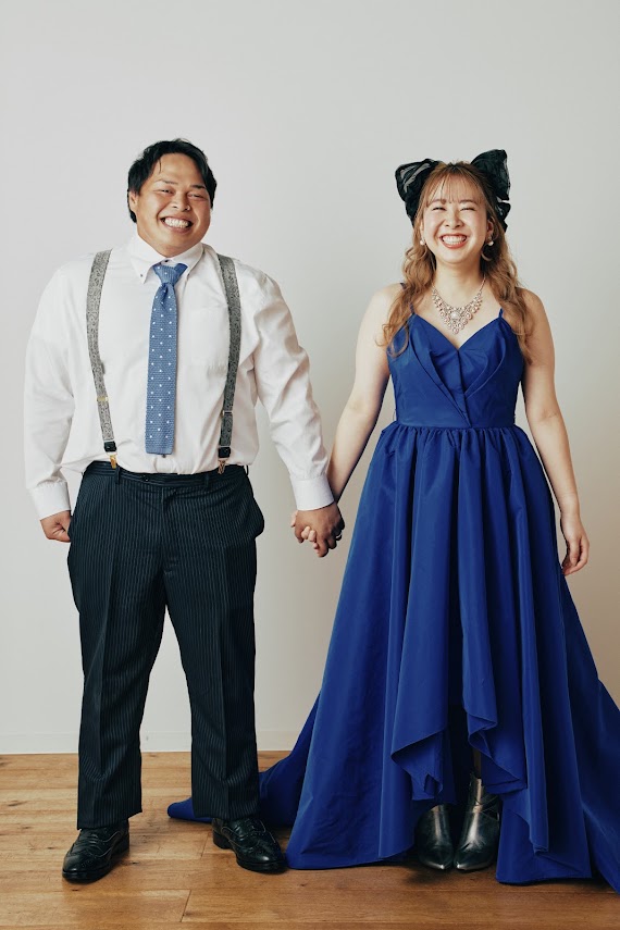 ブルーのドレスとサスペンダースタイルで手をつなぐ新郎新婦