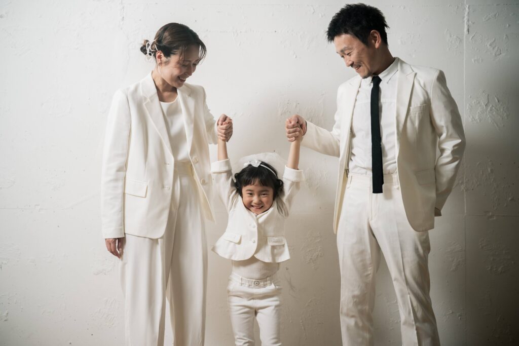 白の衣装で統一し、お子様と手をつなぐご家族のスタジオフォト