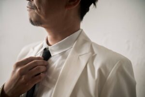 白のジャケットとシャツに黒のネクタイを合わせ、胸元を整える新郎
